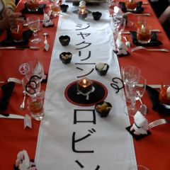 Table harmonie de rouge, blanc et noir, composée d'une nappe rouge, d'un chemin de table  blanc avec inscriptions japonaises noires, de serviettes en forme de lotus noires, de chevalets en forme de personnages accroupis sur tatami et en kimono blanc.