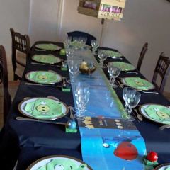 Table composée d'une nappe noire, d'un chemin dominante bleue, peint de paysages façon "jeu pour tablettes", de serviettes vertes "cochon", de chevalets oiseaux sur un socle herbe et d'un centre de table suspendu.